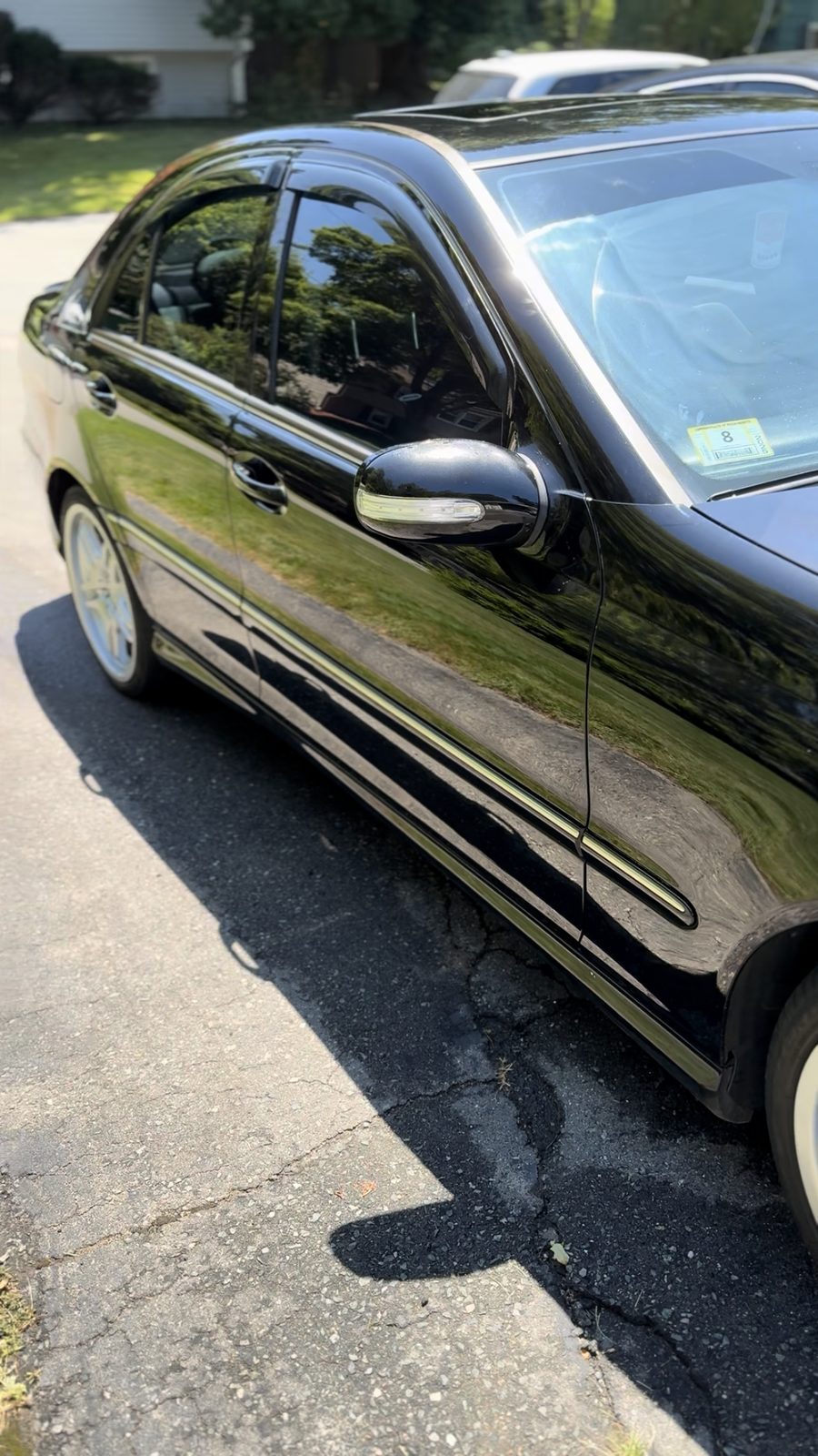 Side profile of a black Mercedes-Benz C-Class with mirror-gloss paint clearly reflecting the surrounding lawn and trees